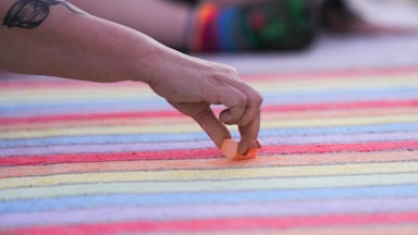 Someone with a flower tattoo on their arm draws a rainbow in chalk.