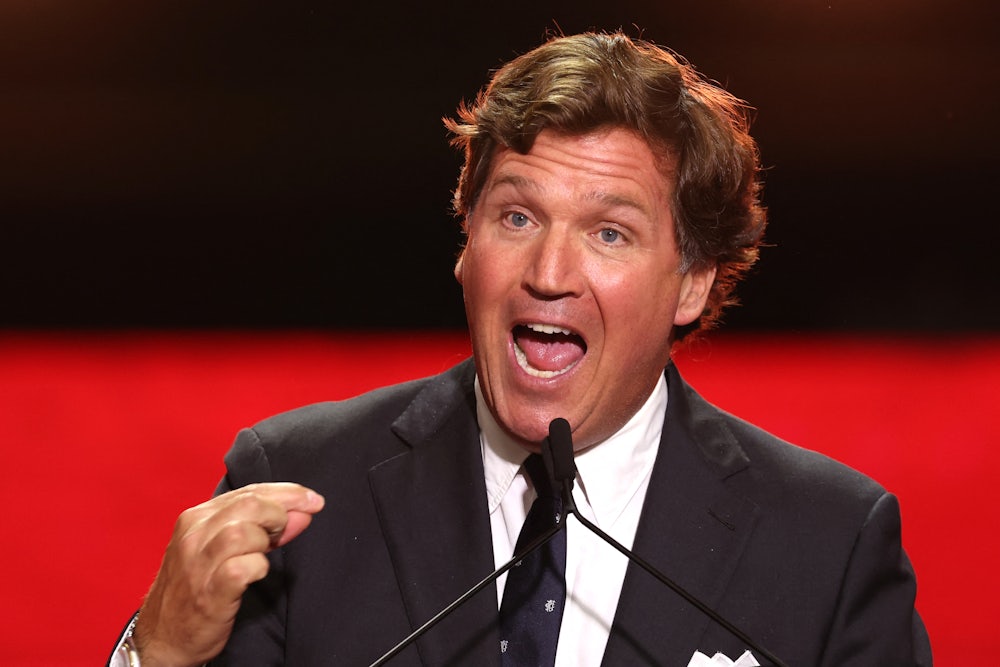 Tucker Carlson gestures while speaking into a microphone