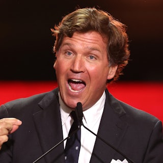 Tucker Carlson gestures while speaking into a microphone