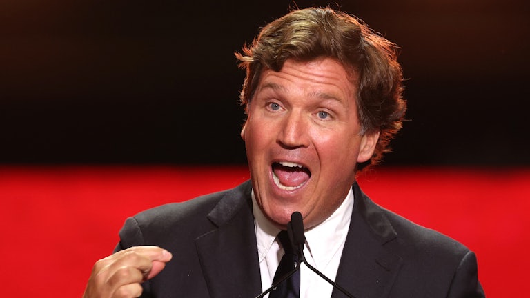 Tucker Carlson gestures while speaking into a microphone