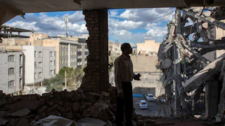 A man stands in a destroyed building in Tehran observing the damage.