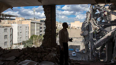 A man stands in a destroyed building in Tehran observing the damage.