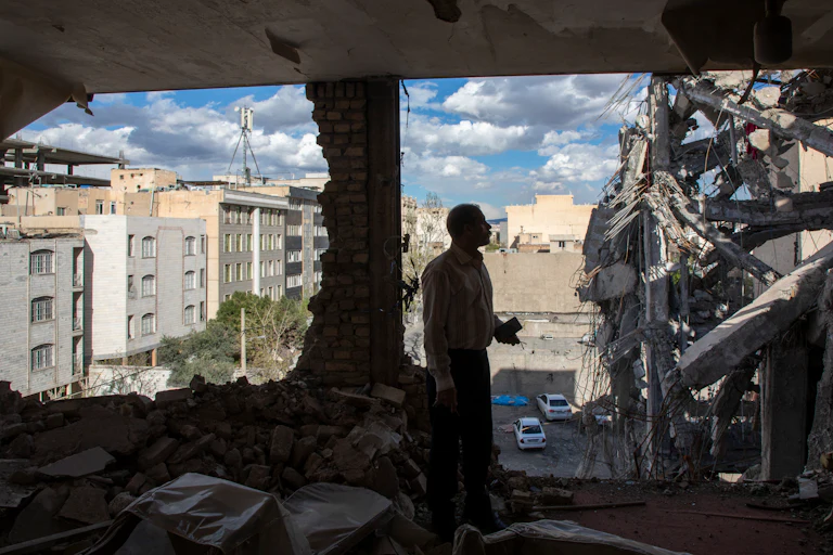 A man stands in a destroyed building in Tehran observing the damage.