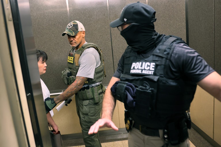 Two men wearing police vests gra a woman in an elevator. One of them is masked.