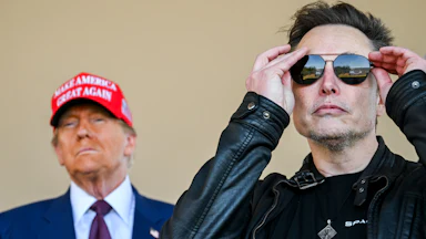 Musk puts on sunglasses while Trump stands behind him