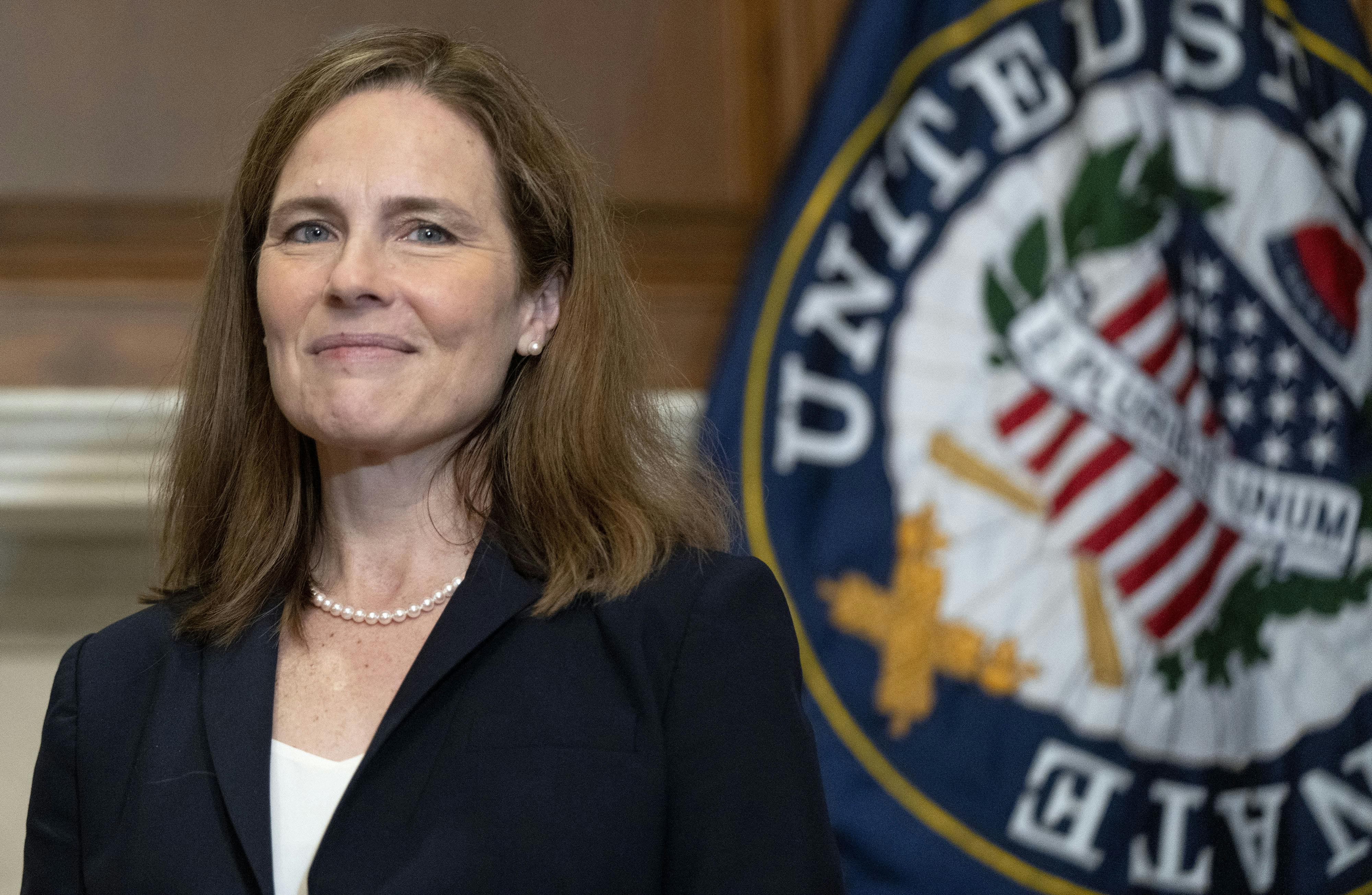 Justice Amy Coney Barret smiles next to the seal of the Supreme Court.