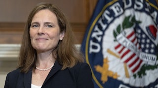 Justice Amy Coney Barret smiles next to the seal of the Supreme Court.