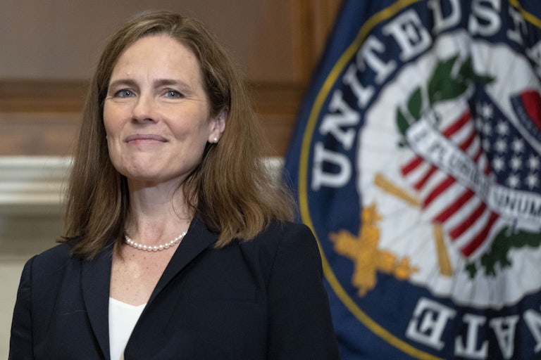 Justice Amy Coney Barret smiles next to the seal of the Supreme Court.