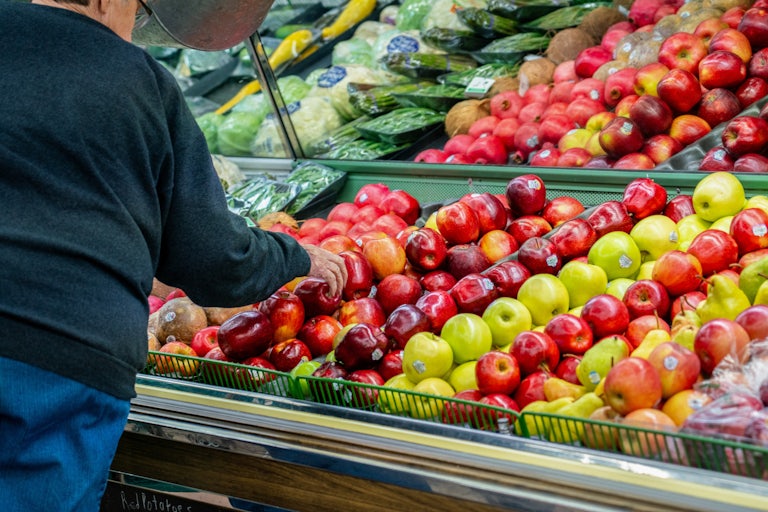 A man leans over to pick an apple at a grocery store.
