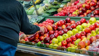 A man leans over to pick an apple at a grocery store.