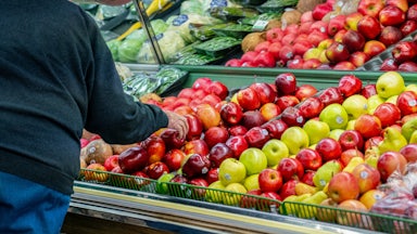 A man leans over to pick an apple at a grocery store.
