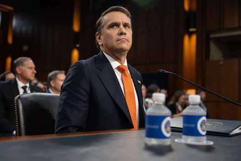 Acting Attorney General Todd Blanche sits at a table in a congressional hearing, two small water bottles before him.