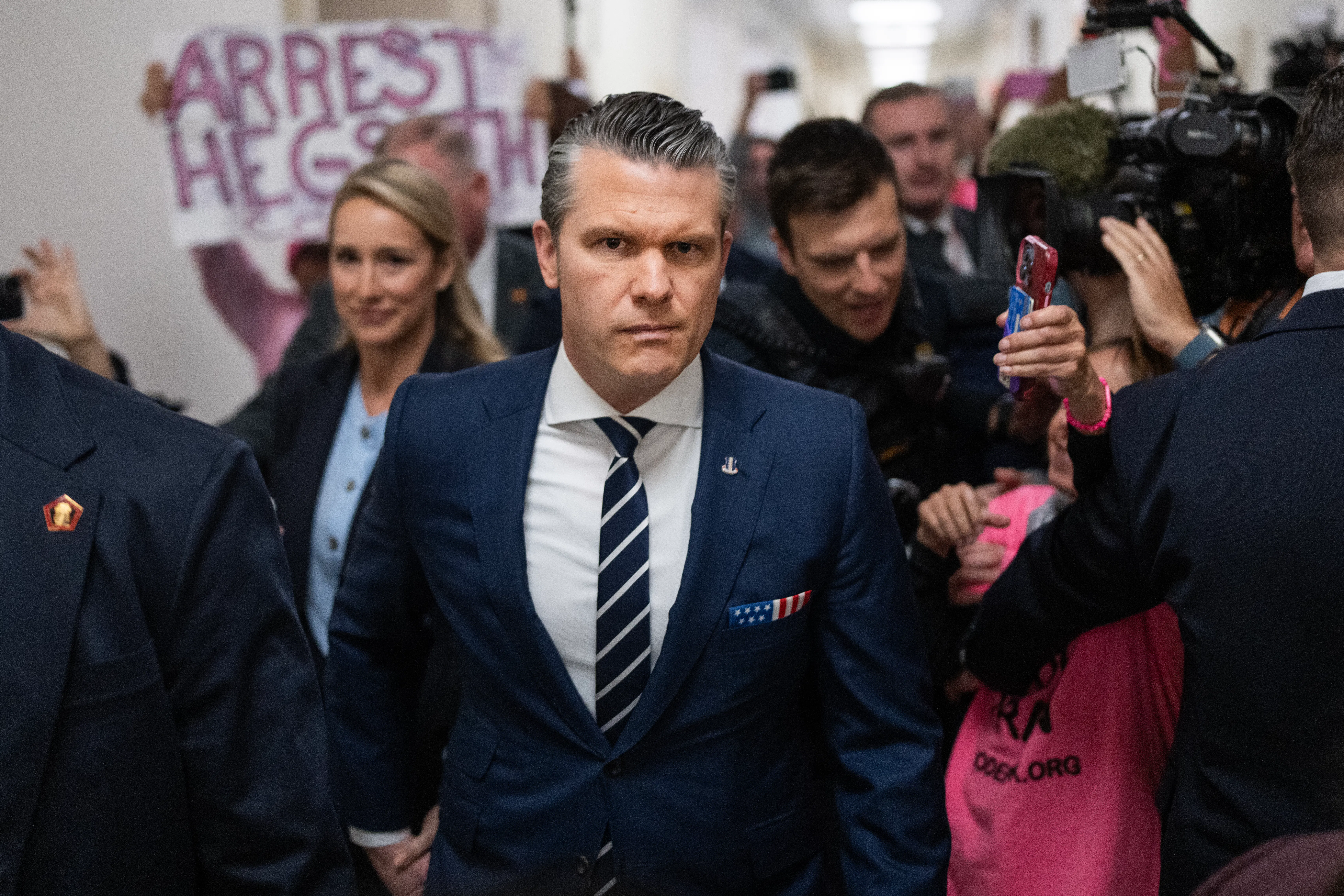 Protesters greet Defense Secretary Pete Hegseth as he prepares to testify before the House Armed Services Committee. One sign reads "Arrest Hegseth."