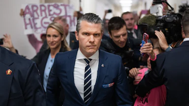 Protesters greet Defense Secretary Pete Hegseth as he prepares to testify before the House Armed Services Committee. One sign reads "Arrest Hegseth."
