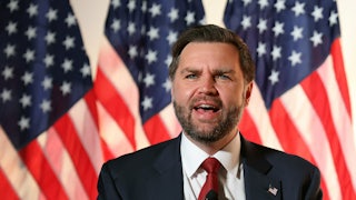Vice President JD Vance speaks into a microphone while standing in front of American flags