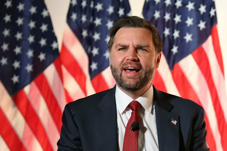 Vice President JD Vance speaks into a microphone while standing in front of American flags