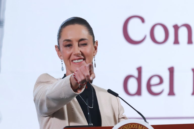 Mexican President Claudia Sheinbaum winks and points while standing at a podium during a press conference