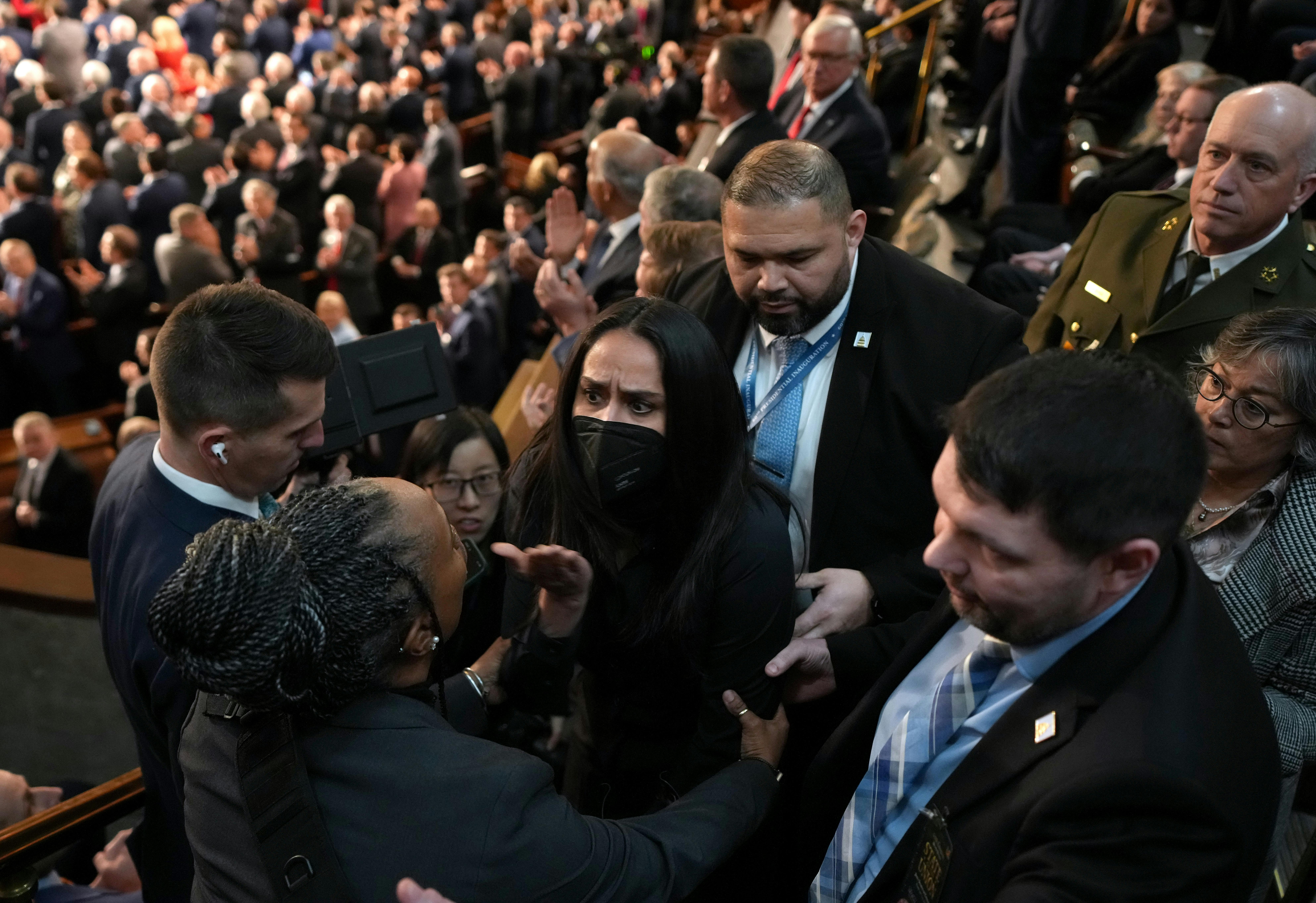 Aliya Rahman, wearing a face mask, is surrounded by people trying to escort her out of Trump's State of the Union.