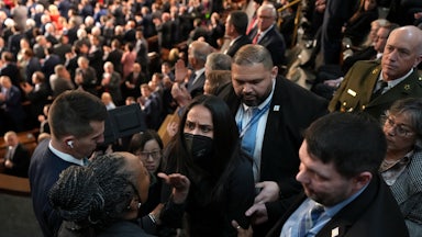 Aliya Rahman, wearing a face mask, is surrounded by people trying to escort her out of Trump's State of the Union.