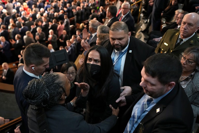 Aliya Rahman, wearing a face mask, is surrounded by people trying to escort her out of Trump's State of the Union.