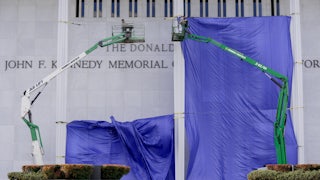 Workers add Donald Trump’s name on the facade of the Kennedy Center while a blue tarp hangs over much of the building.