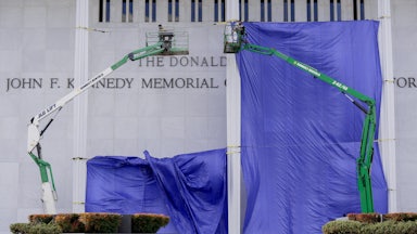 Workers add Donald Trump’s name on the facade of the Kennedy Center while a blue tarp hangs over much of the building.