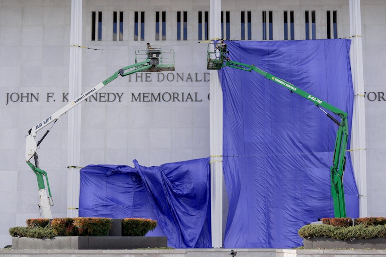 Workers add Donald Trump’s name on the facade of the Kennedy Center while a blue tarp hangs over much of the building.