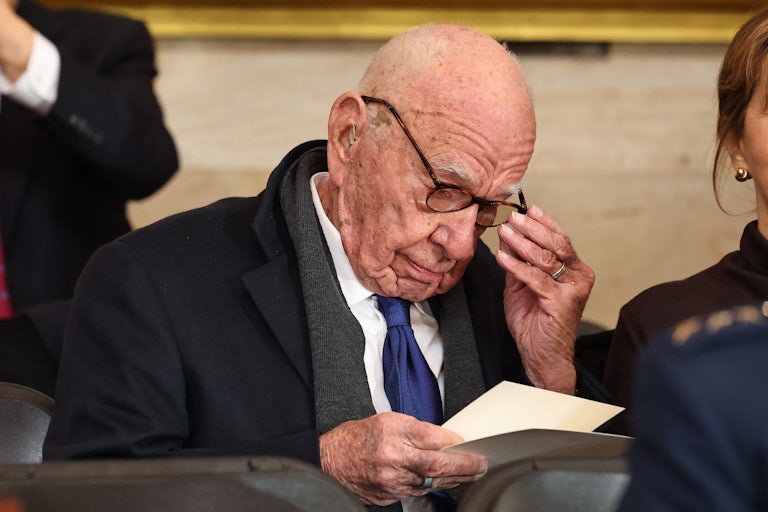 Rupert Murdoch adjusts his glasses as he reads a piece of paper in his hands while seated at Donald Trump's inauguration.