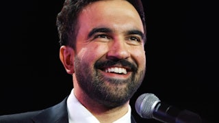 New York City Mayor-elect Zohran Mamdani smiles while standing at a microphone
