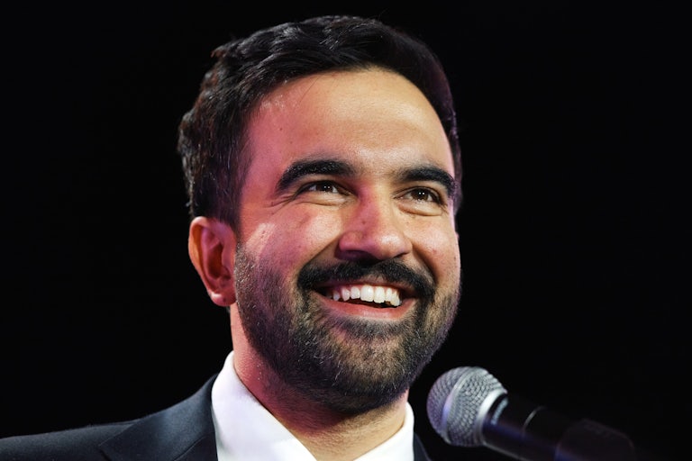 New York City Mayor-elect Zohran Mamdani smiles while standing at a microphone
