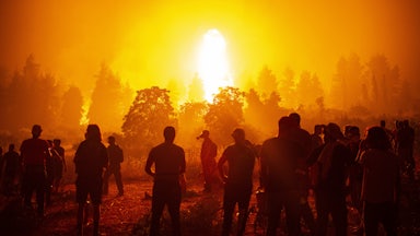 People stand in front of a raging wildfire.