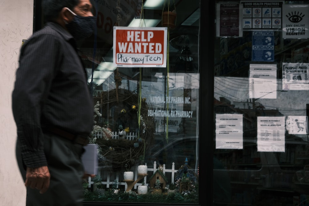 A masked man walks past a help wanted sign on a storefront window.