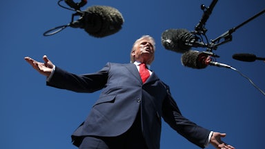 Donald Trump holds his arms out to the side while speaking into microphones
