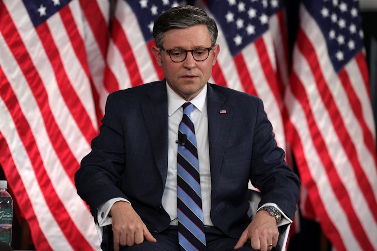 Mike Johnson, seated, looks down. U.S. flags are behind him.