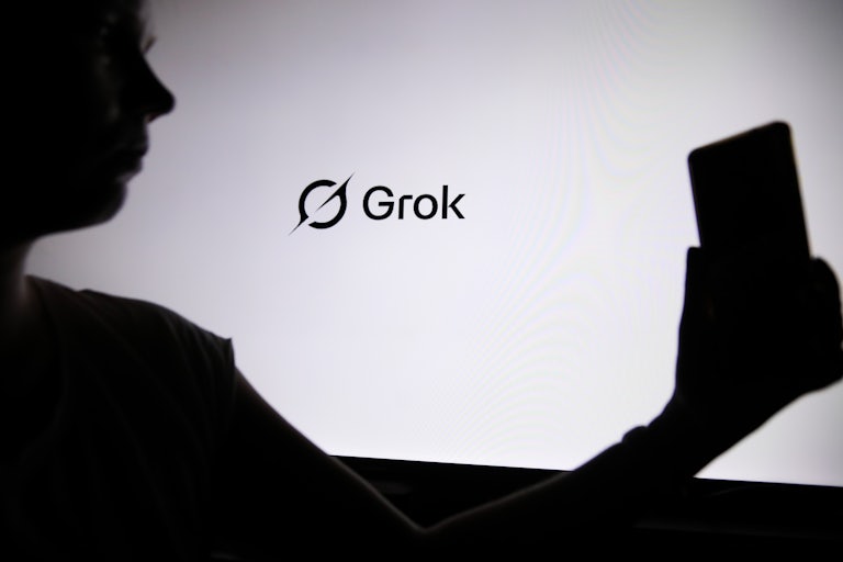 Someone in silhouette holds a phone in front of a Grok banner.