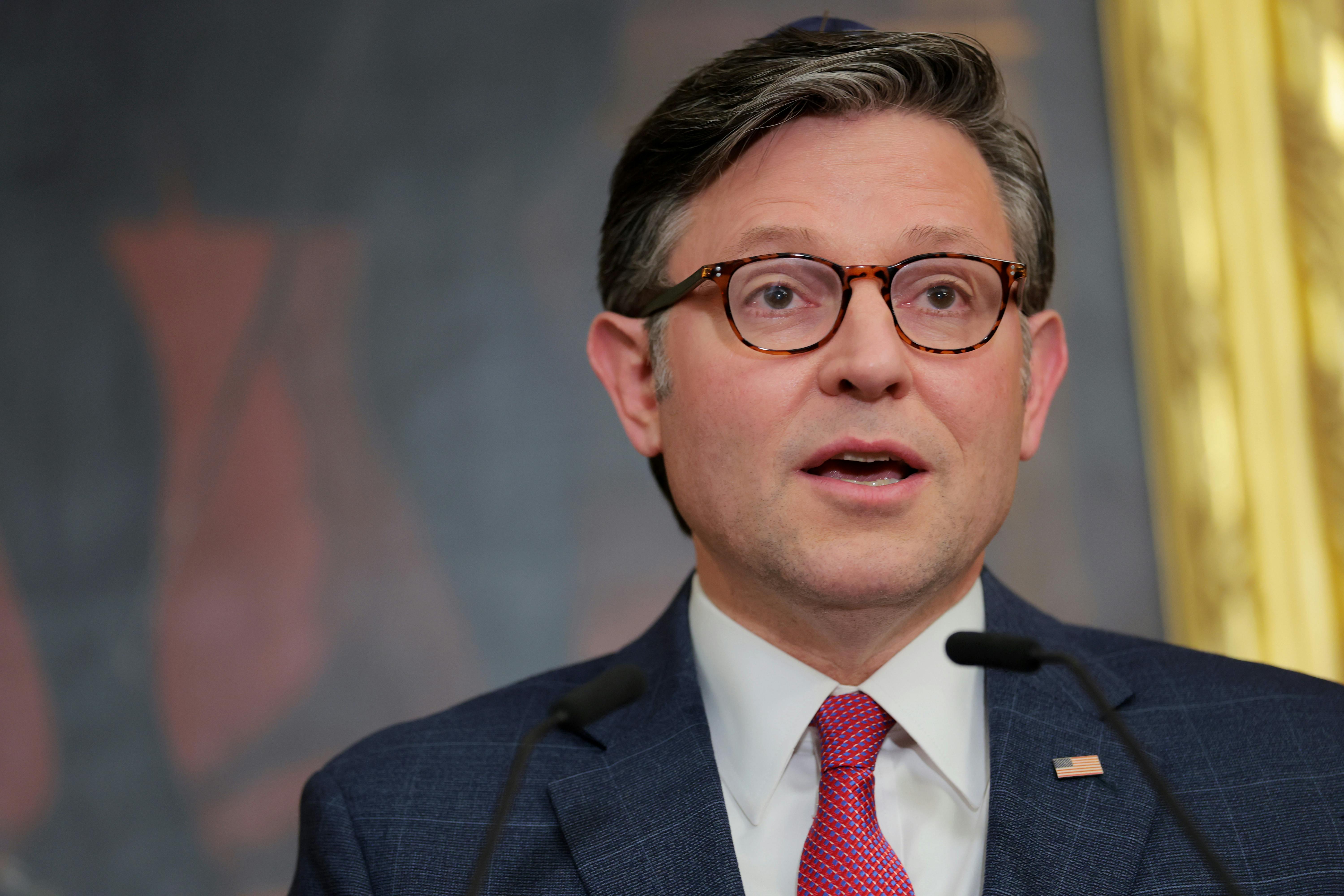 House Speaker Mike Johnson looks shocked while speaking at a lectern.