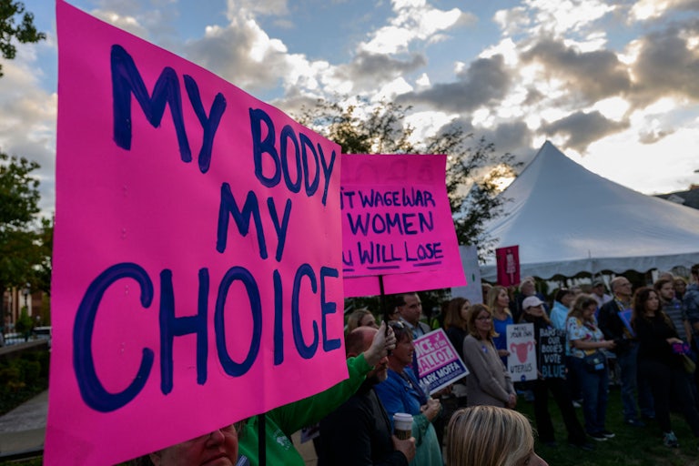 An abortion rights protest with dozens of people in the photo. A large pink sign in the foreground reads "My body my choice." Another in the background threatens that "You will lose" if you wage war with women. (Part of the text is cut off.)