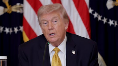 President Donald Trump speaks while seated at a table with the presidential seal.