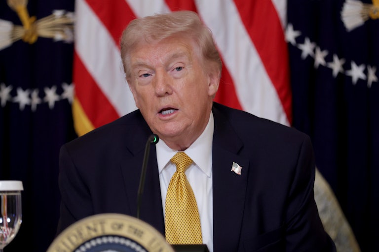 President Donald Trump speaks while seated at a table with the presidential seal.