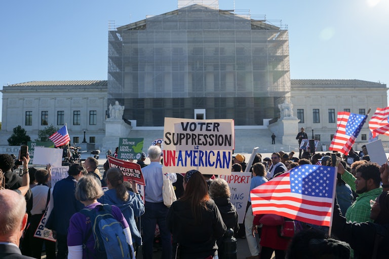 Protesters hold up U.S. flags and a sign that reads "Voter Suppression is Unamerican" while standing in front of the Supreme Court.