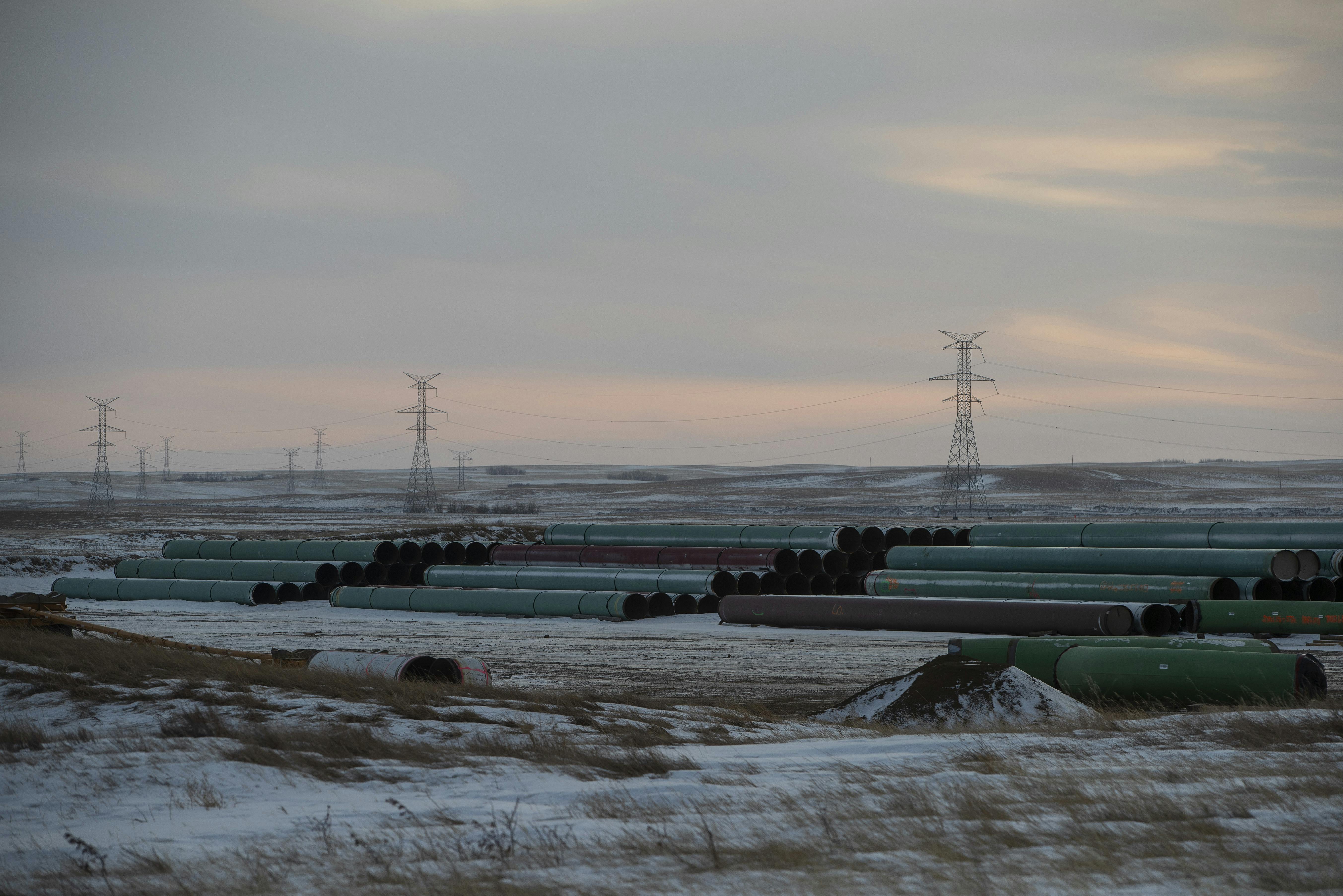 Pipes lie on the frozen prairie with power lines in the background.
