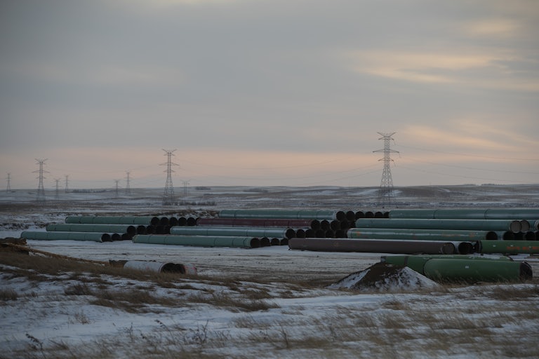 Pipes lie on the frozen prairie with power lines in the background.