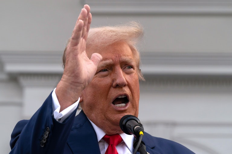 Donald Trump points his hand in the air and yells. A mic is near his mouth.
