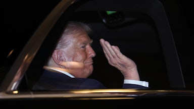 Donald Trump waves while sitting in the back of a car
