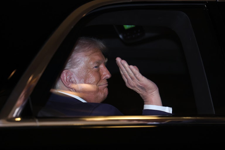 Donald Trump waves while sitting in the back of a car