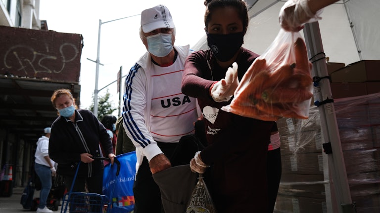 A masked couple collects carrots at a food bank. 