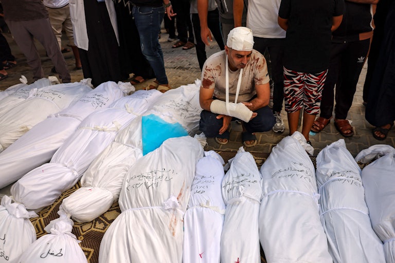 Injured Palestinian Mahmoud Al-Areer stands near the corpses of his children lying among other bodies