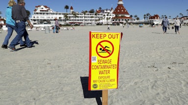 A photograph of a sign in front of the iconic Hotel del Coronado in Coronado, California, warns of contaminated ocean water.