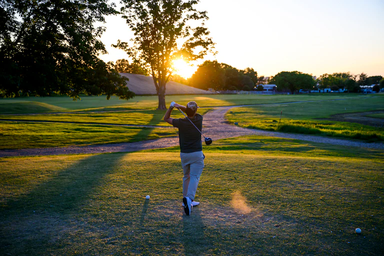 A man swings his golf club at East Potomac Golf Links