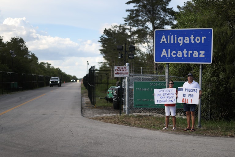 Two protesters stand below a sign reading "Alligator Alcatraz," near the detention center.